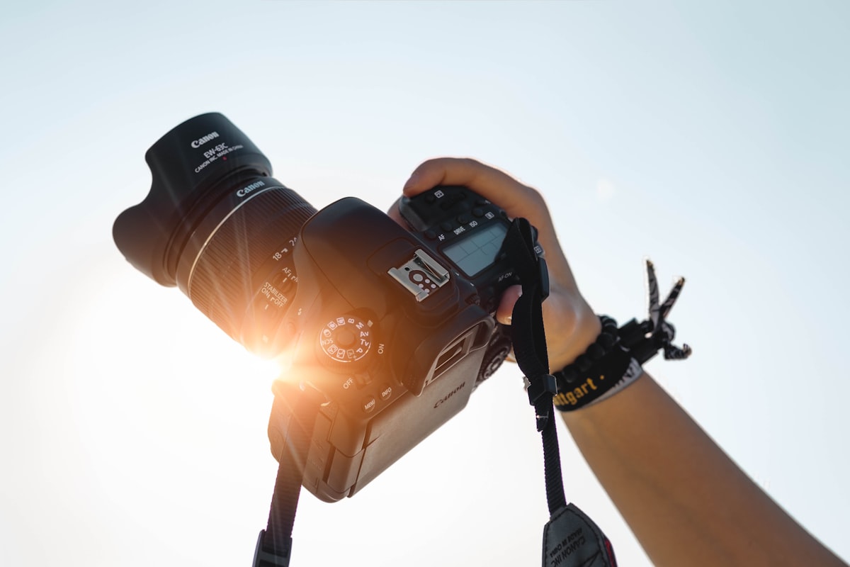 Photographer holding a professional DSLR camera with golden sunlight flaring through the lens